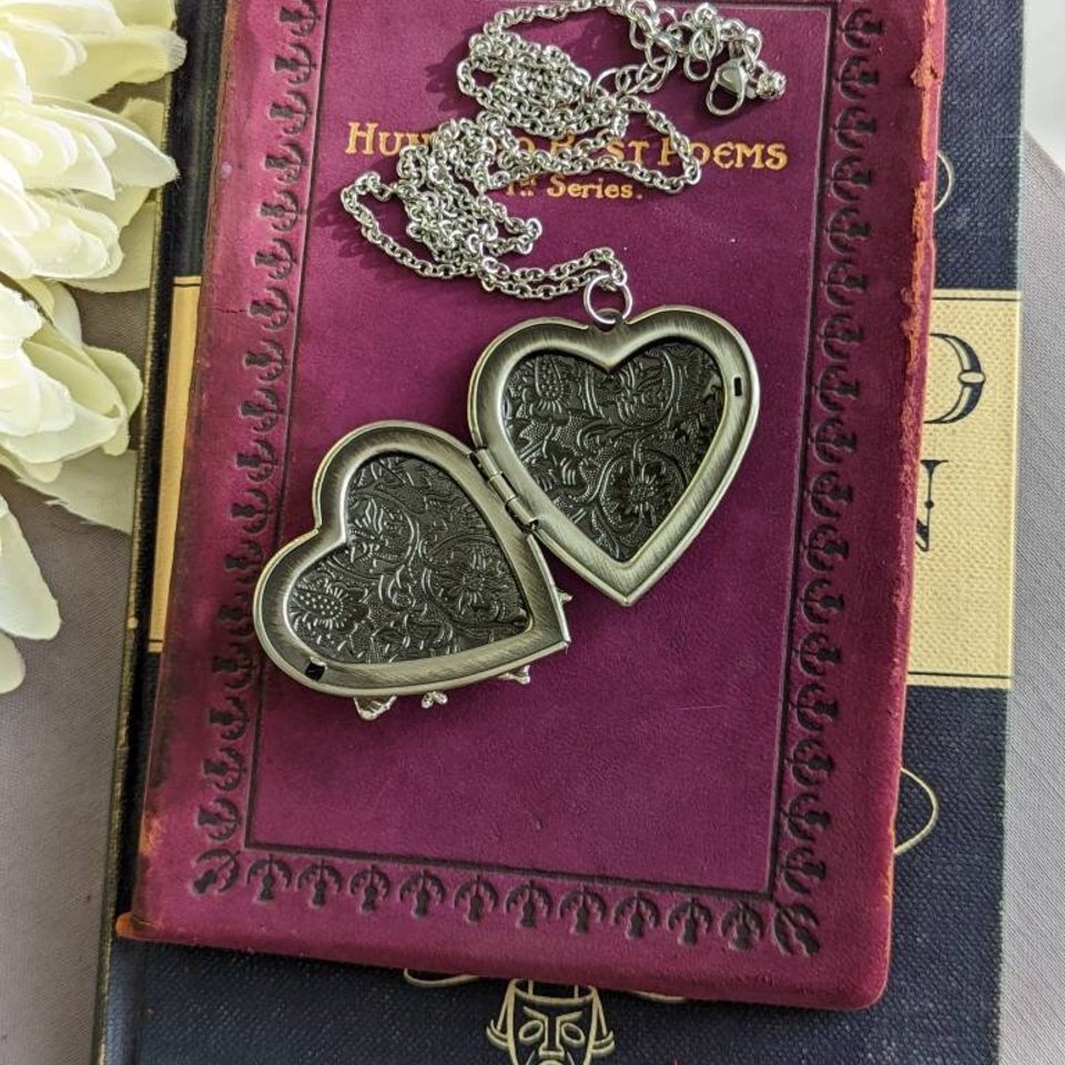 Open Silver Heart locket is displayed on a purple vintage book.