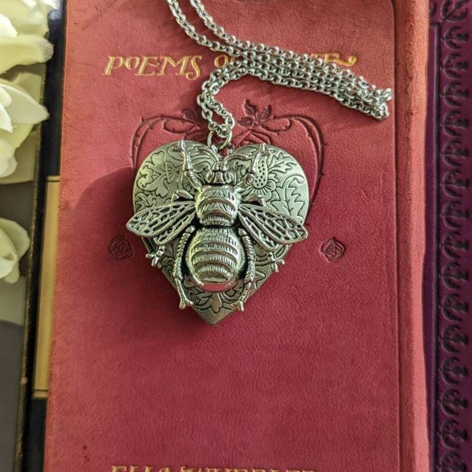 Silver Heart locket with floral design and large bee embellishment on top. Locket is displayed on a red vintage book.